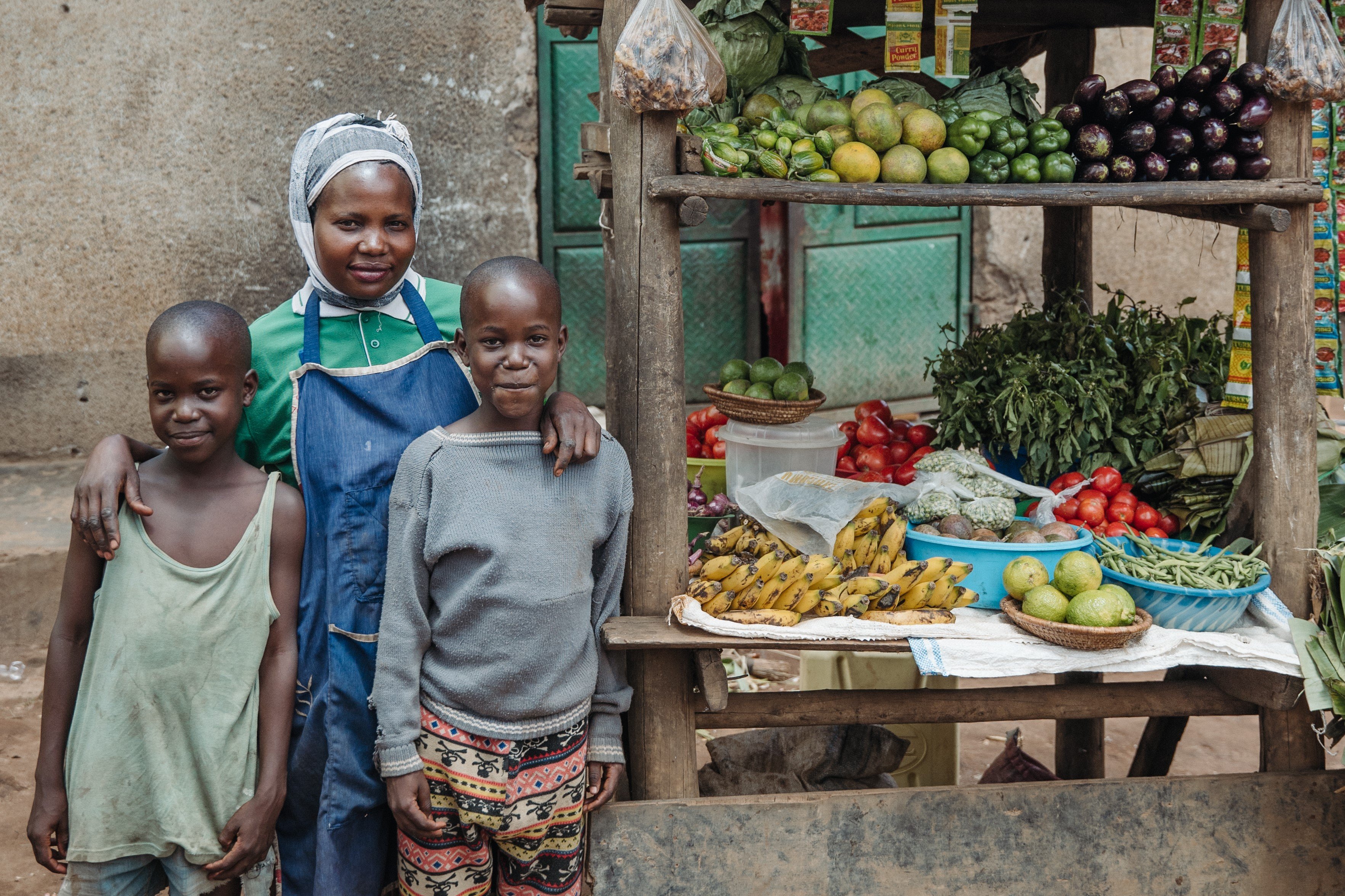 Young mother in apron next to a produce stand, arms around two children