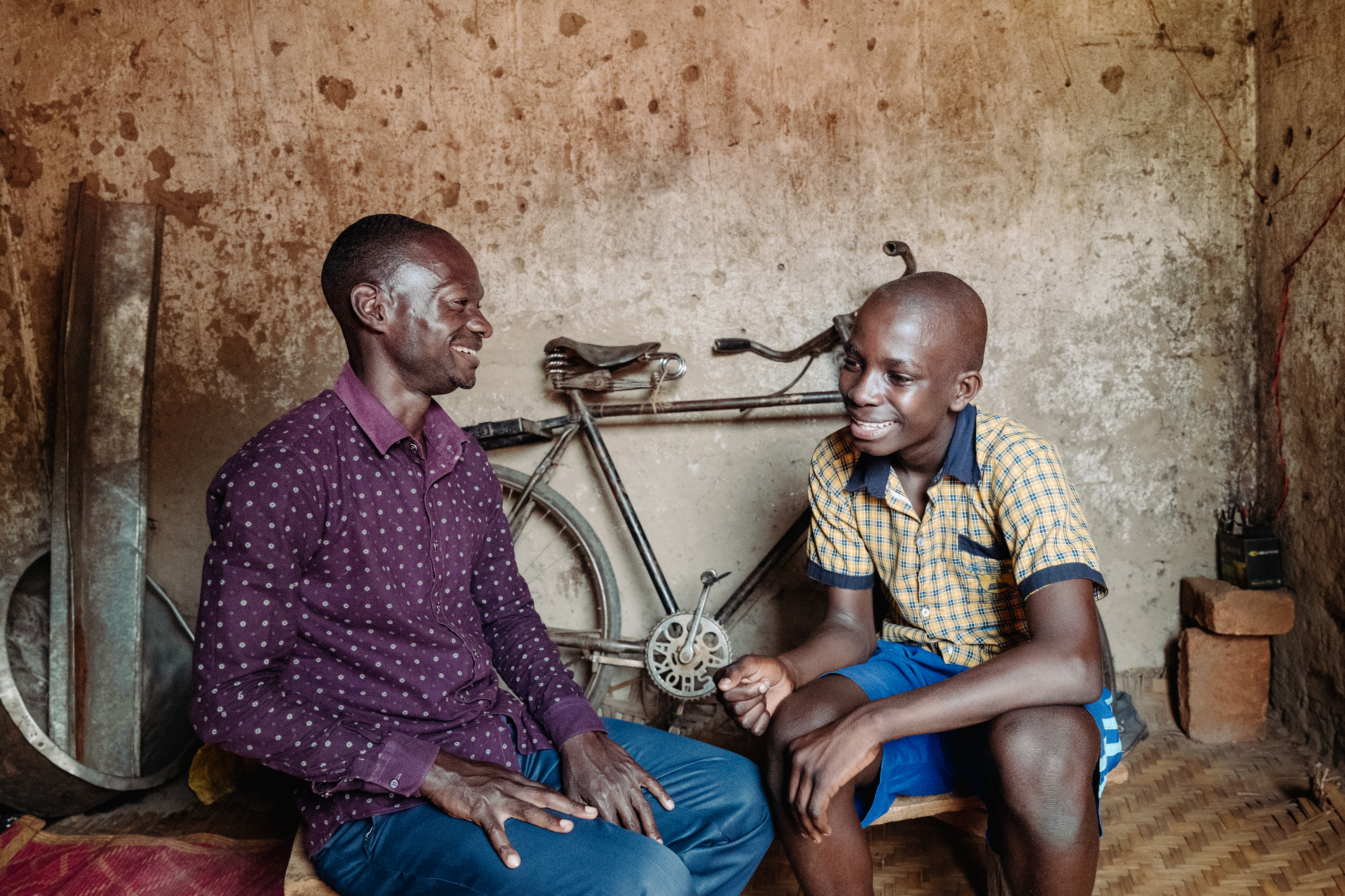 Younger man talking to boy, smiling, bicycle in background