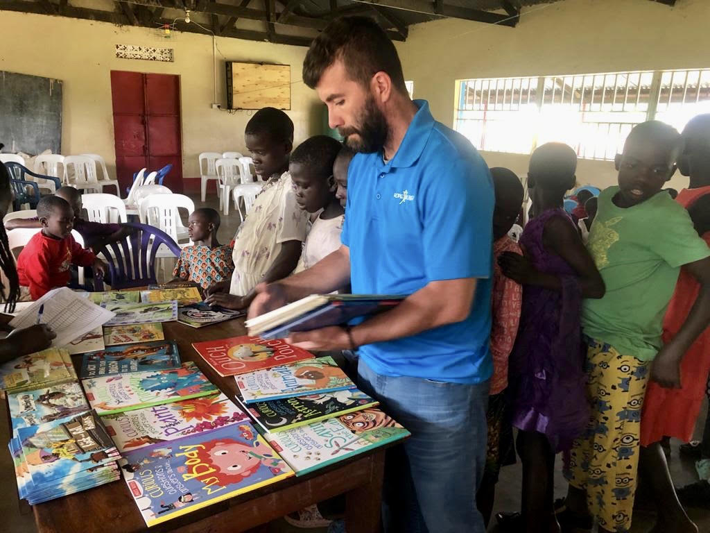 Michael sorting books Man with crowd of children in front of table with children's books
