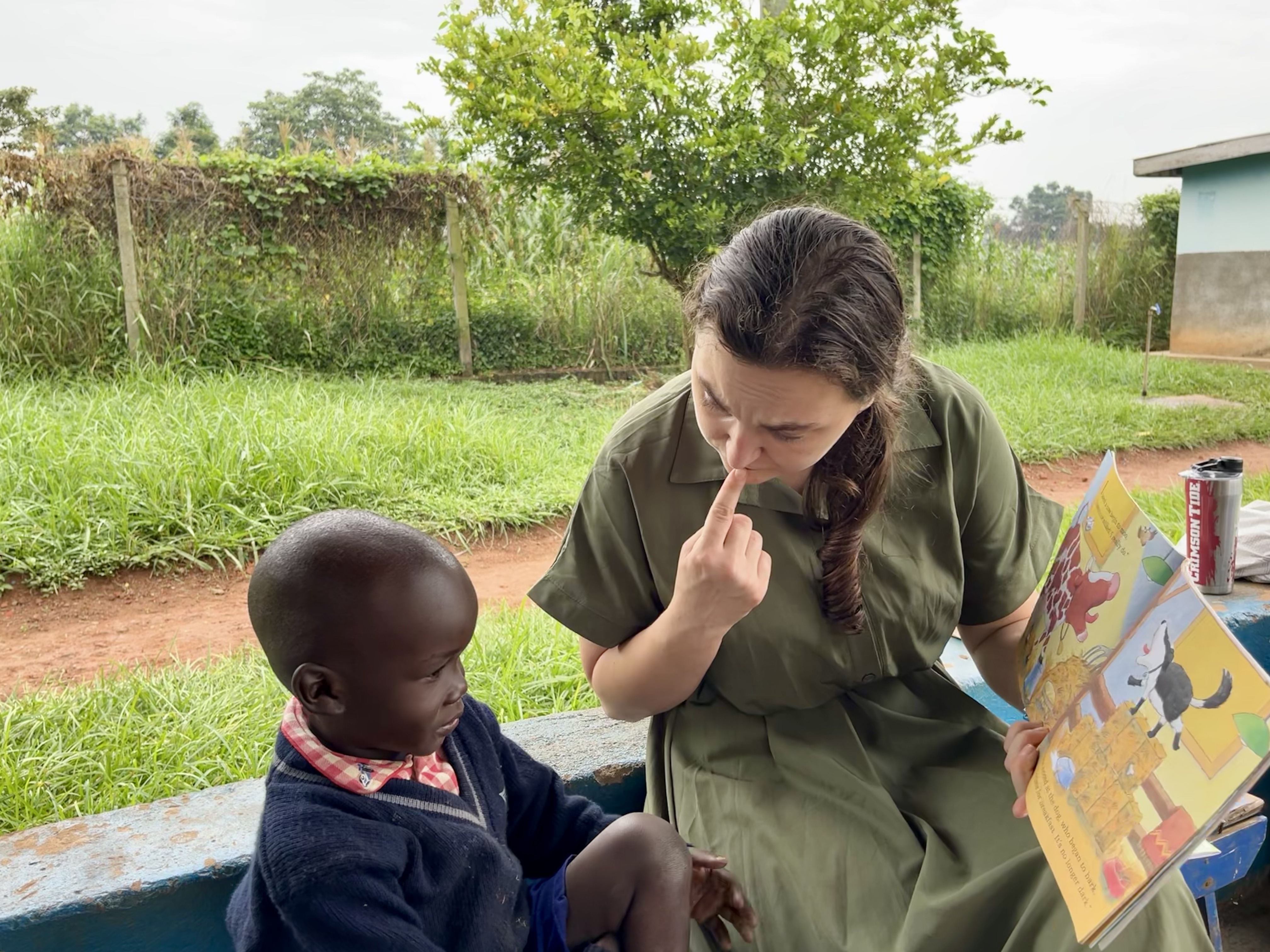 American woman talking to Ugandan child, pointing to her own nose
