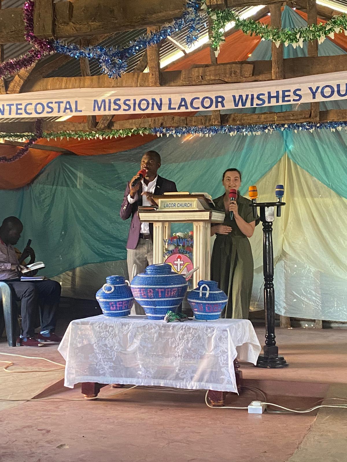 Ugandan man and American woman on a church stage holding microphones