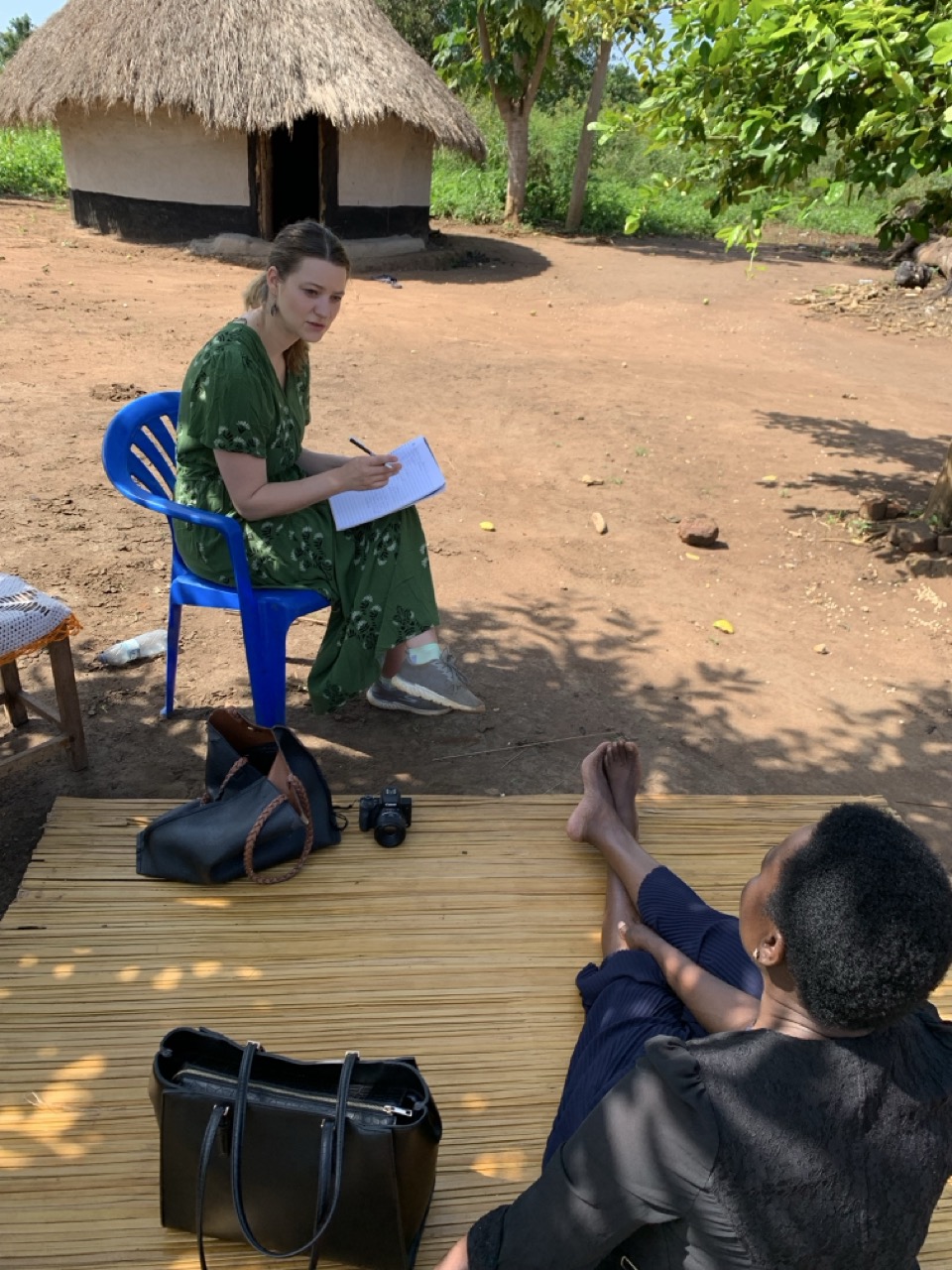 Bianca collecting stories in Uganda American woman with notebook in front of hut